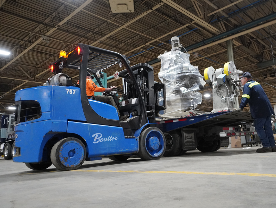 Forklift lifting specialized spring manufacturing equipment off trailer.