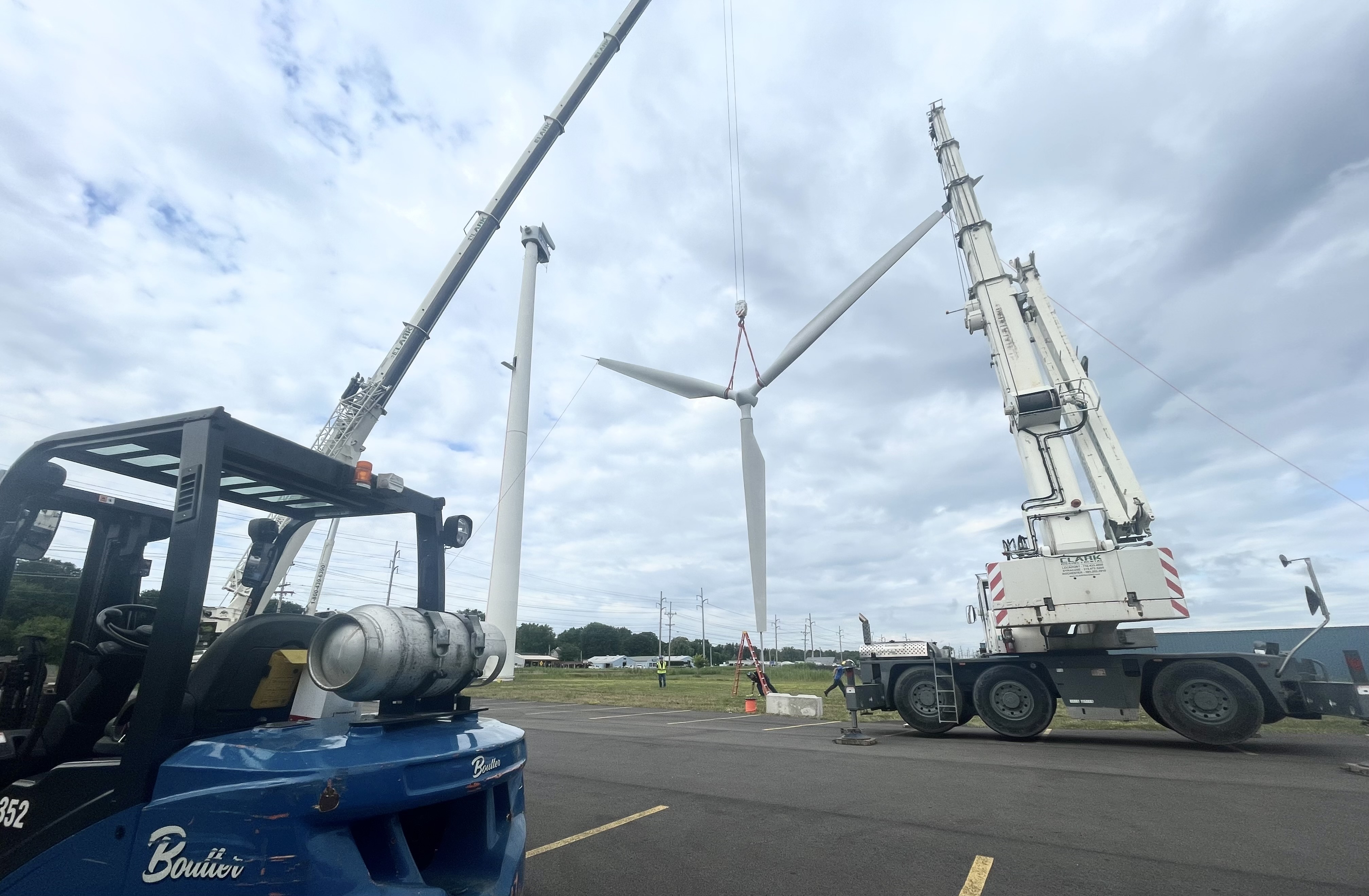 Two large cranes lifting wind turbine blades to remove inside nacelle